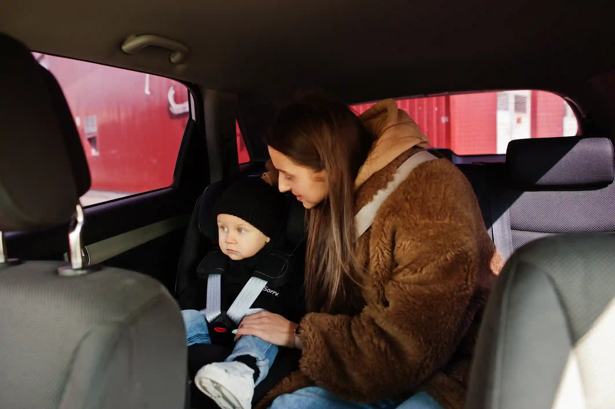 Une mère assise sur le siège passager d'une voiture, avec son enfant solidement attaché à l'arrière, tous les deux profitant d'un trajet conduit par le chauffeur en toute sécurité.